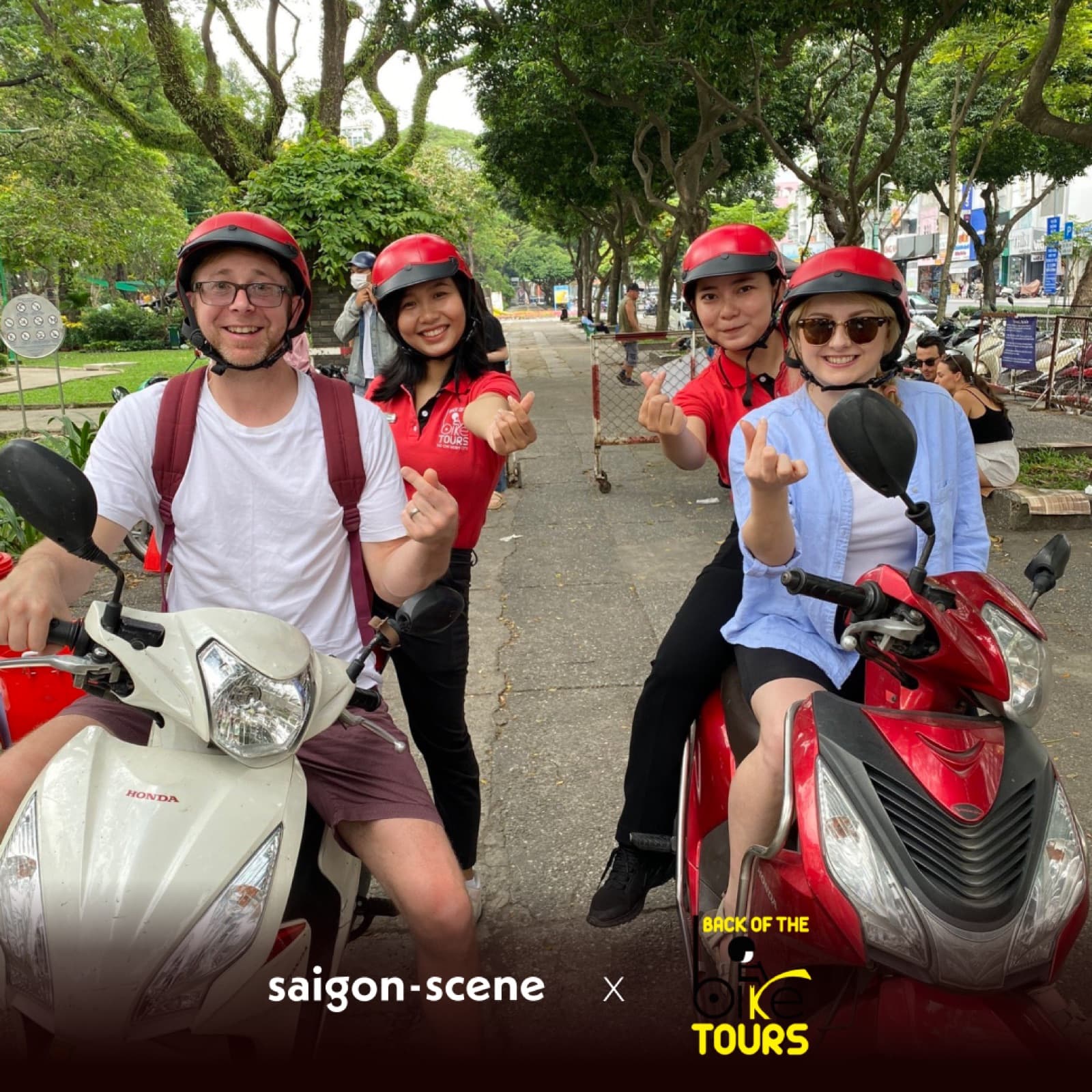 Riders in red helmets grinning on two scooters at the start of a Back of the Bike tour